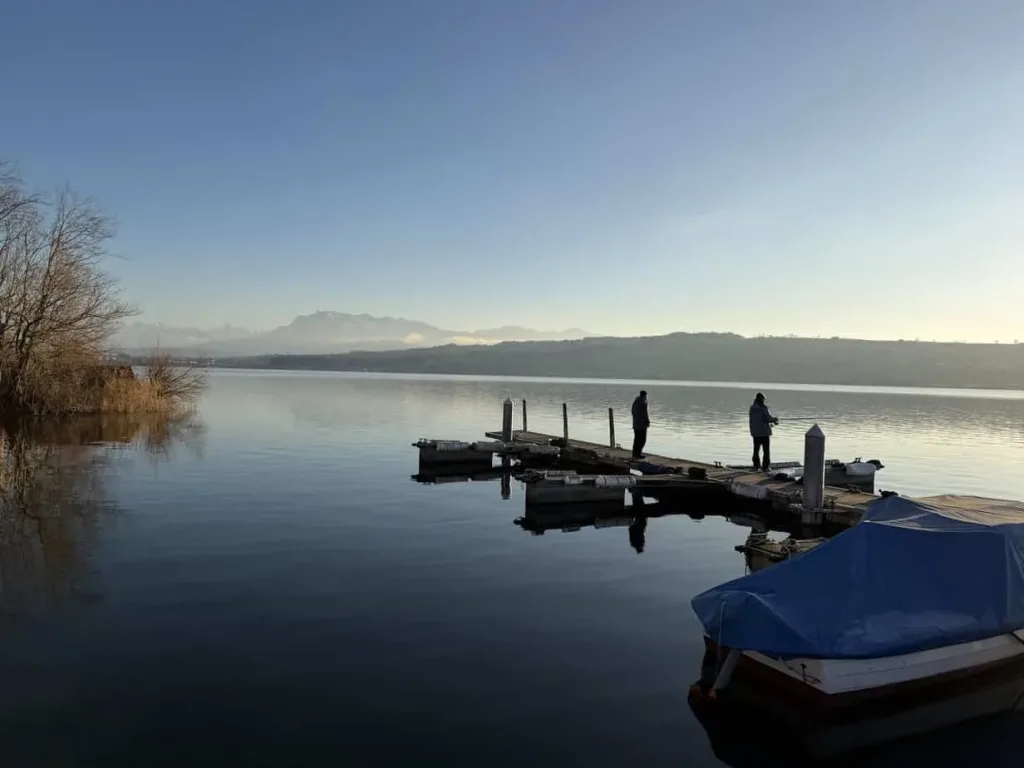 Hafen am Fluss mit Anglern, ruhige Wasseroberfläche bei Sonnenaufgang, Naturkulisse, Entspannung und Freizeit.
