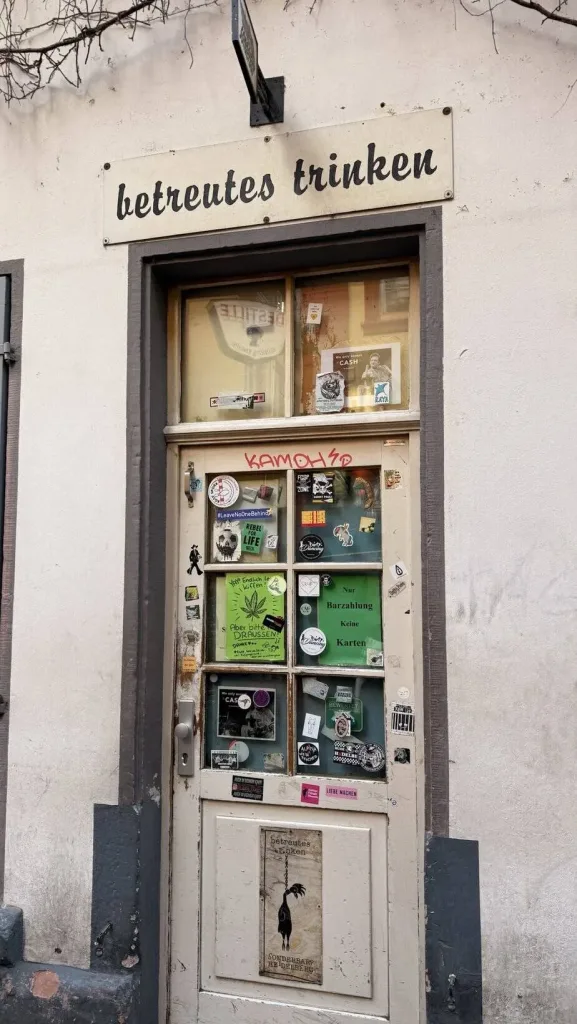Altes Türschild mit "betreutes trinken" in Schwarz, urbaner Shots mit Streetart-Charme.