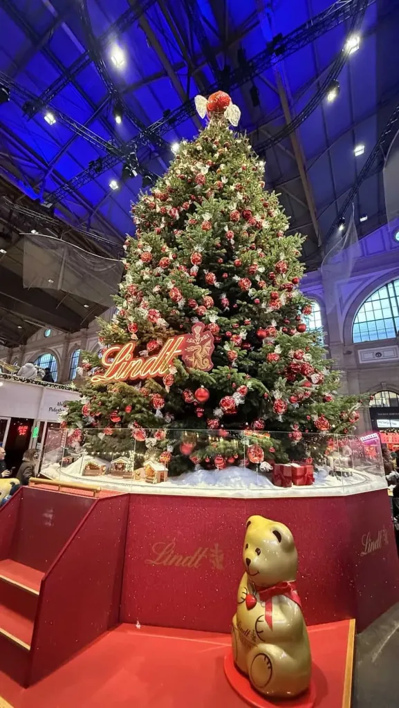 1. Weihnachtsbaum mit roten Dekorationen bei Lindt, festliche Stimmung im Innenraum.