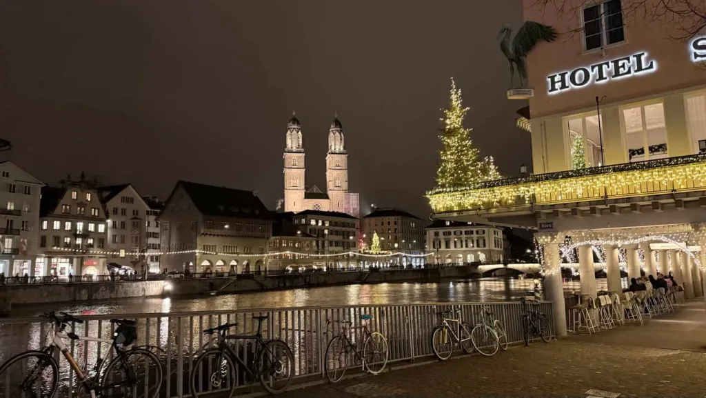 Gemütliche Winternacht in Zürich mit festlicher Beleuchtung und Weihnachtsdekorationen am Flussufer.