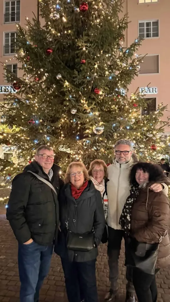 Glückliche Menschen vor Weihnachtsbaum mit Beleuchtung und Ornamenten in festlicher Stimmung.