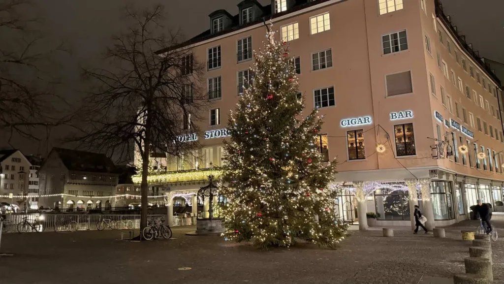 Festlich geschmückter Weihnachtsbaum vor Hotel im Stadtzentrum, winterliche Atmosphäre, Weihnachtsdekoration, urbane Silhouette.