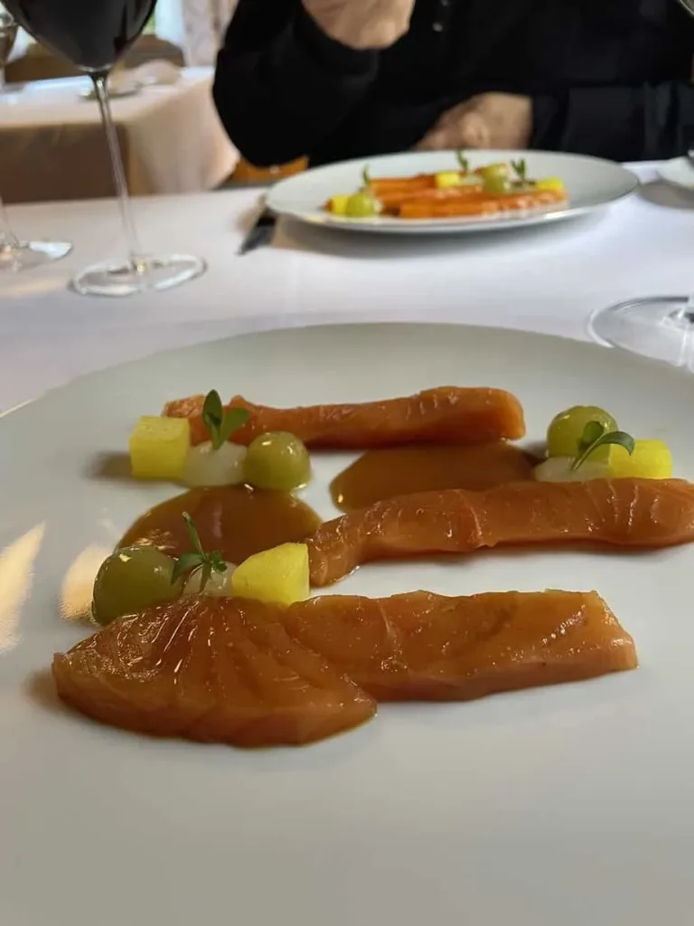 Zarter Räucherlachs mit Mango und grünen Trauben auf weißem Teller, elegante Präsentation im feinen Restaurant.