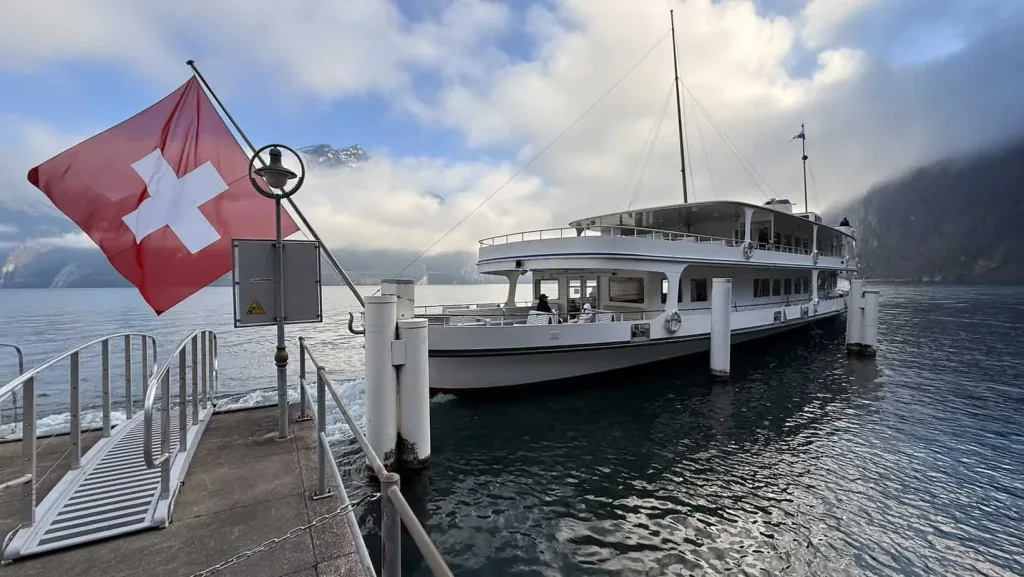 Schweizer Flagge auf Boot am Vierwaldstättersee vor Bergen und Wolkenhimmel, malerischer Schweizer See.
