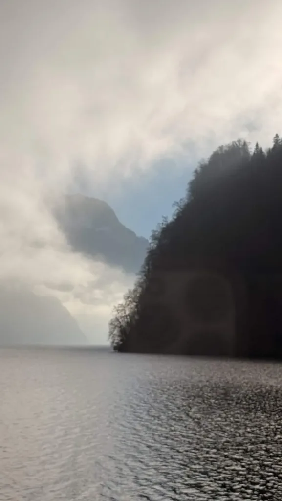 Alte See- und Felsenlandschaft mit Nebel, ruhigem Wasser und bewachsenen Klippen.